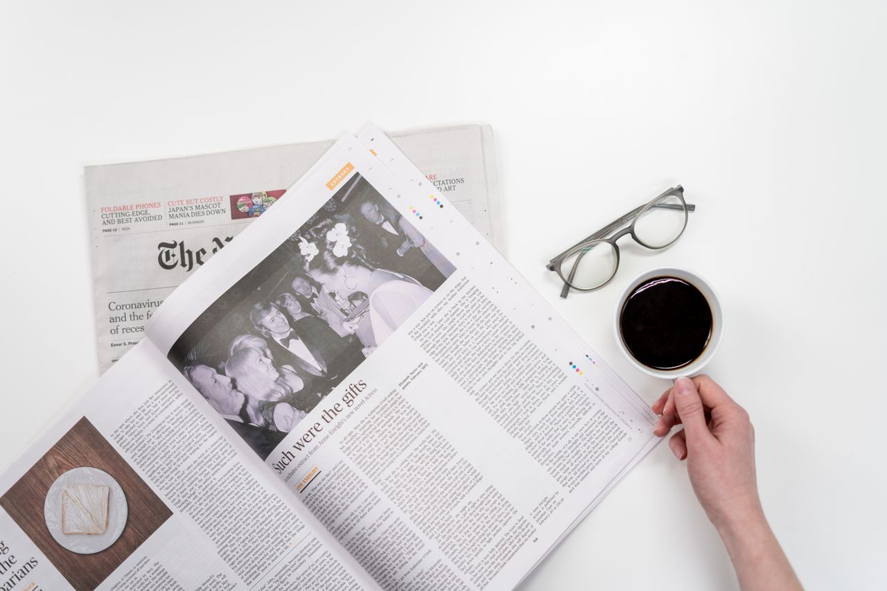 services-img Overhead view of newspaper reading with coffee and glasses on a white table.