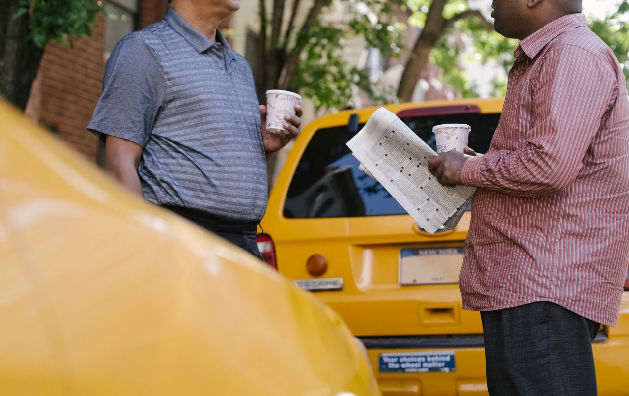 services-01 Crop anonymous multiracial taxi drivers with takeaway coffee and newspaper speaking near yellow cars in town