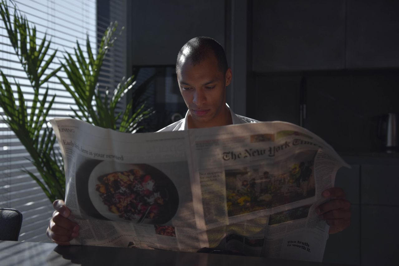 services-02 Businessman focused on reading newspaper in a sunny indoor office setting.